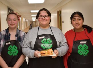 Three students posing with a plate of food with a sandwich on it.